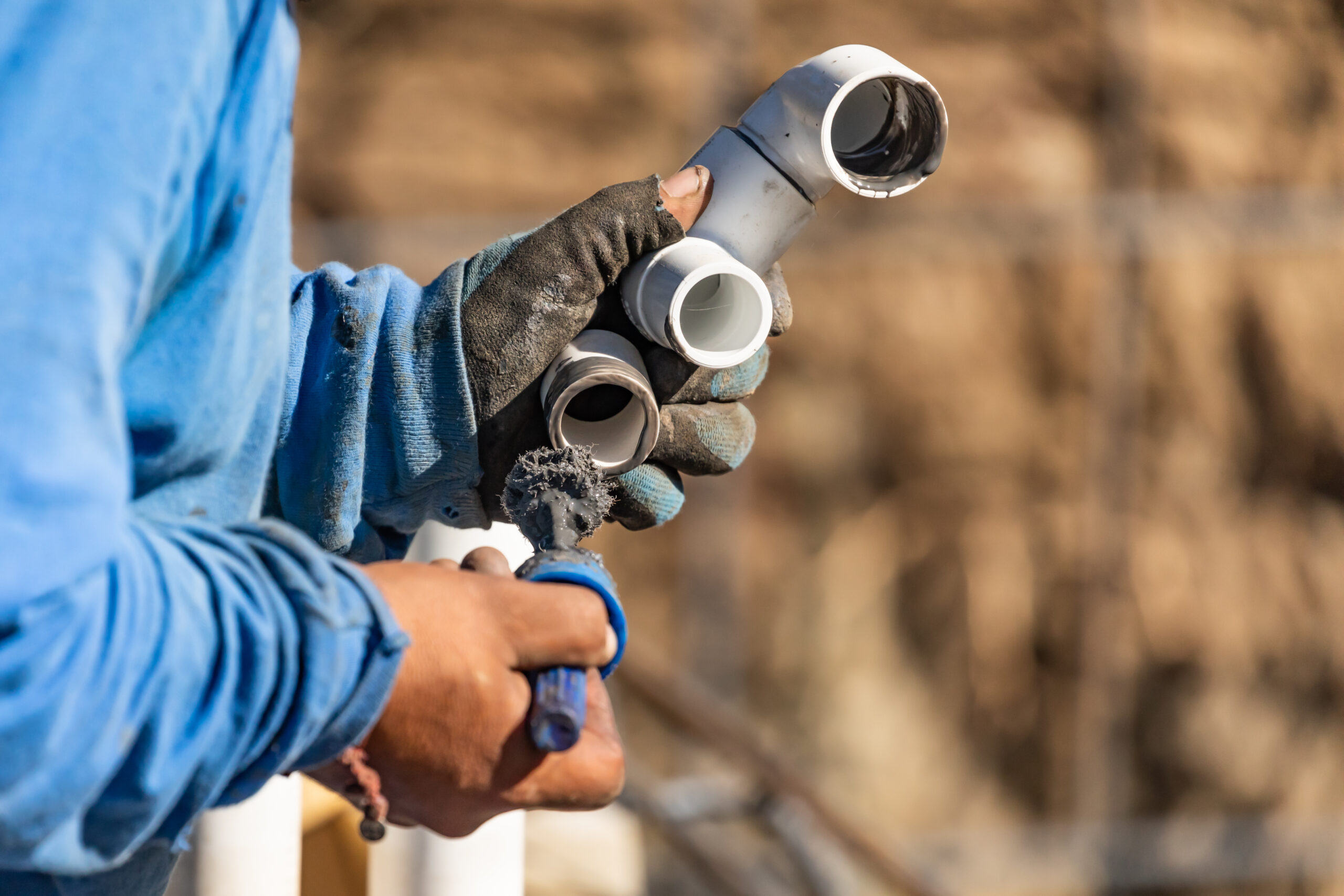 Plumber Applying Pipe Cleaner, Primer and Glue to PVC Pipe At Construction Site