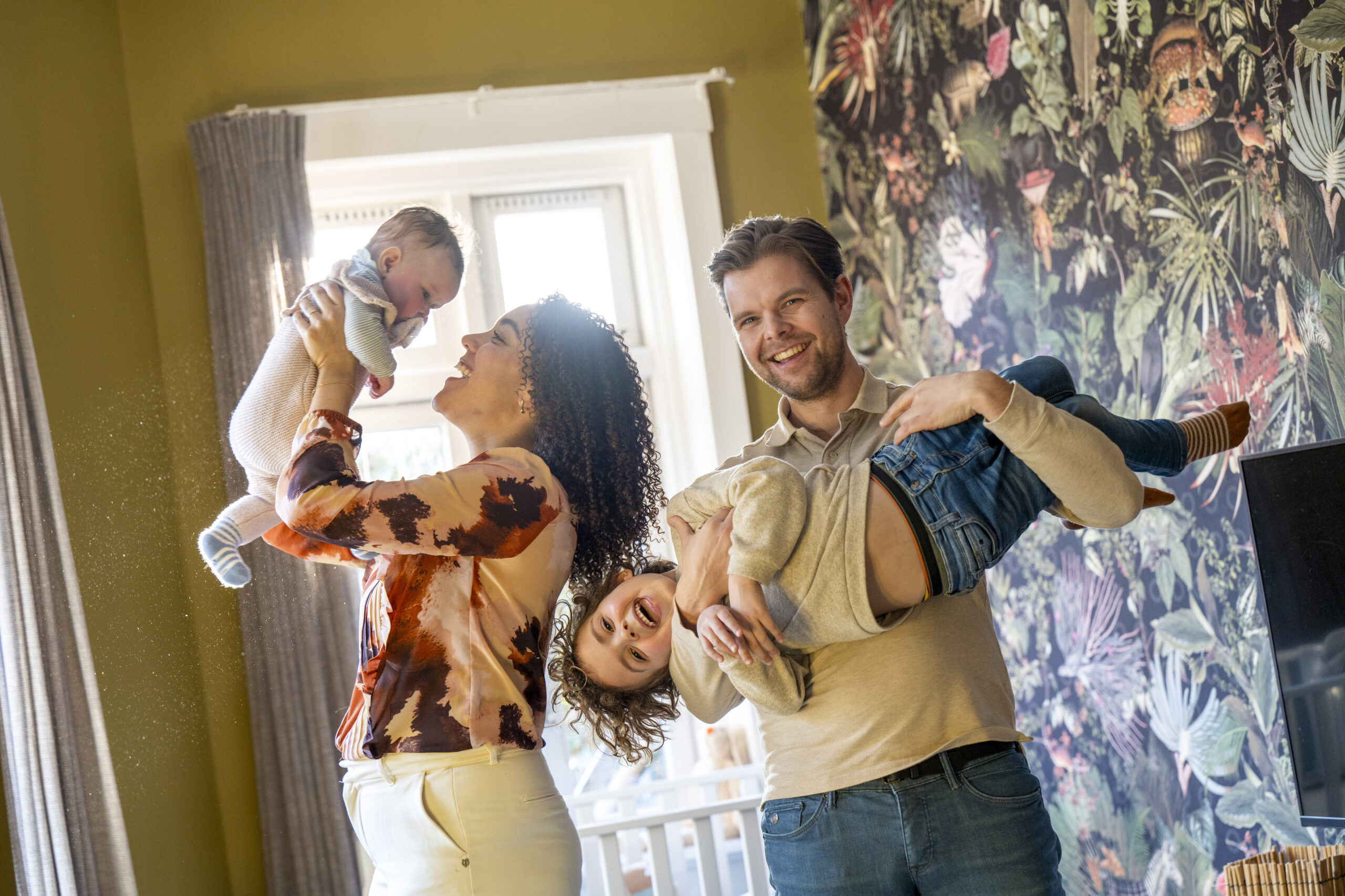 Family fun time with playful parents lifting happy children in a sunlit home